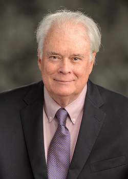 Bucky Kilbourne wearing a suit jacket and red tie in front of a dark background