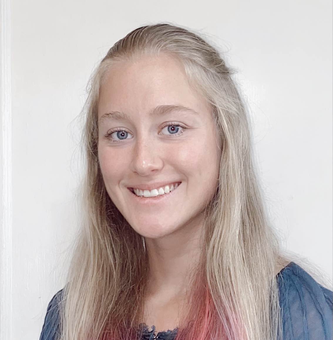 A woman with blonde hair that is pink at the tips in a blue shirt.